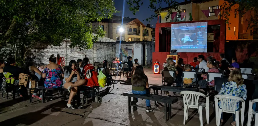 El público sentado en el patio mira el escenario montado frente a la casa, con guirnaldas colgadas.