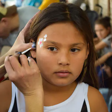 Nena mira a cámara mientras le terminan de pintar la cara.