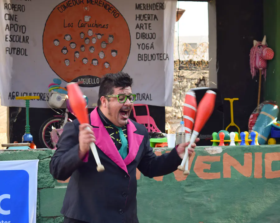Un artista hace malabares con clavas sobre el escenario del patio.