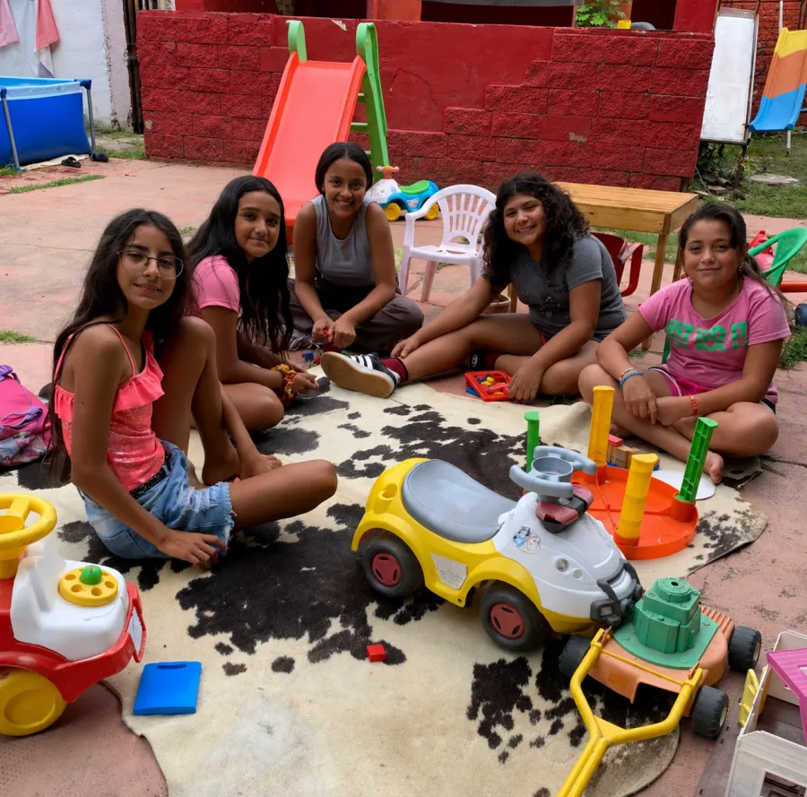 Un grupo de chicas sentadas en el patio, jugando entre autitos y juguetes.